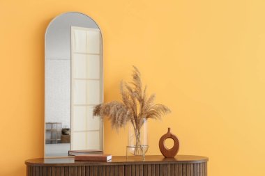 Odadaki sarı duvarın yanındaki çekmecelerde ayna ve otlar, yakın plan.