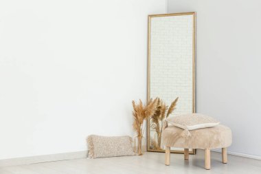 Zemin aynası, puf ve vazo. Beyaz duvarın yanında otlar var.