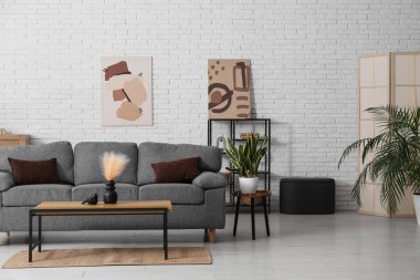 Rahat gri kanepesi ve beyaz tuğla duvarın yanındaki masası olan oturma odasının içinde.