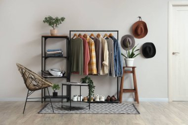 Farklı kıyafetlerle, raf ünitesiyle, beyaz duvarın yanındaki masa ve koltukla dizilin.