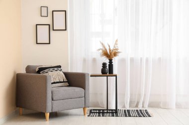 Büyük pencerenin yanında gri koltuklu ve masalı aydınlık oturma odasının içi.