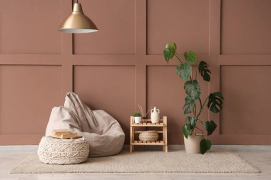 Poufs, ev bitkisi ve raflar odanın içindeki kahverengi duvarın yanında.