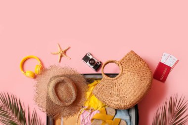 Pembe arka planda giysi ve plaj aksesuarlarıyla dolu bavul, yakın plan.