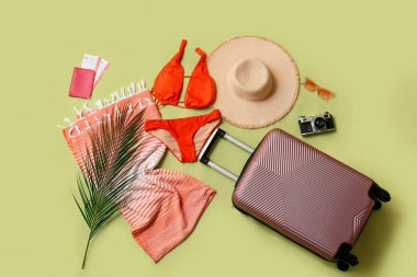 Çantalı kompozisyon, mayo, fotoğraf makinesi ve yeşil arka planda plaj aksesuarları.