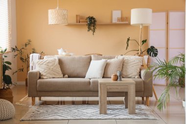 Bej duvarın yanında rahat kanepesi, masası ve çiçekleri olan şık bir oturma odası. Yakın plan.