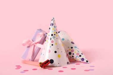 Parti şapkalı kompozisyon, hediye kutusu ve pembe arka planda ıslıklar, yakın plan.