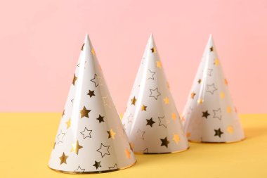 Pembe arkaplan yakınındaki sarı masada parti şapkalı kompozisyon, yakın plan.