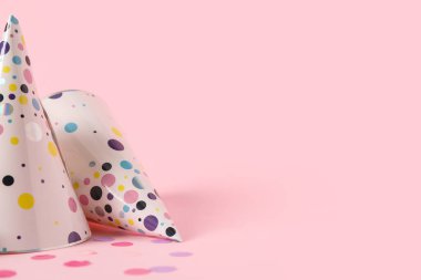 Pembe arka planda parti şapkaları ve konfeti, yakın plan.