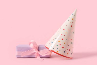 Parti şapkaları ve hediye paketi pembe arka planda, yakın plan.