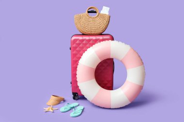 Bavul, şişirilebilir yüzük ve eflatun arka planda plaj aksesuarları.