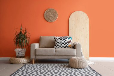 Oturma odasının içinde rahat bir kanepe, puf ve çiçek var.