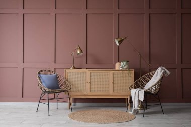 Oturma odasının iç tarafındaki kahverengi duvarın yanında sandık, koltuk ve zemin lambası.