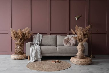 Rahat bir kanepe, puflar ve vazolar, oturma odasının iç tarafındaki kahverengi duvarın yanında otlar.