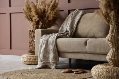 Oturma odasındaki kahverengi duvarın yanında rahat bir kanepe, puf ve terlikler.