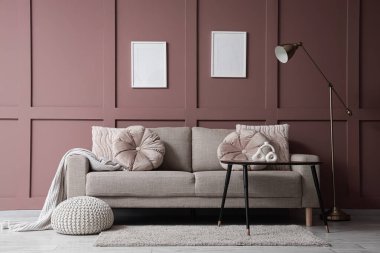 Rahat bir kanepe, masa ve zemin lambası oturma odasının içindeki kahverengi duvarın yanında.