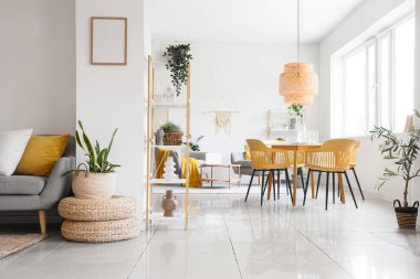 Poufs, raf ünitesi, masa, sandalye ve ev bitkileri odanın içinde.