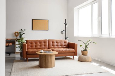 Rahat kahverengi kanepesi, çiçekleri ve ahşap masası olan oturma odasının içinde.