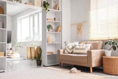 Rahat bej kanepesi ve pencerenin yanındaki raf ünitesi olan oturma odasının içinde.