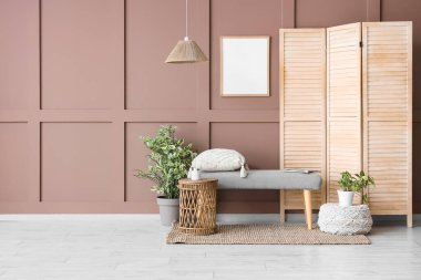 Oturma odasının iç tarafındaki kahverengi duvarın yanındaki benç, katlanan ekran ve bitkiler.