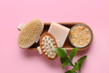 Tepsi, masaj vücut fırçası, sabun ve kase ile kompozisyon pembe arka planda deniz tuzu, yakın plan