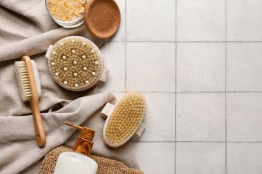 Masaj vücut fırçaları, eldiven, deniz tuzu ve beyaz karo arka planda bir şişe kozmetik ürünü ile kompozisyon