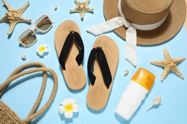 Şık plaj ayakkabıları, aksesuarları ve mavi arka planda bir şişe güneş kremi olan kompozisyon.