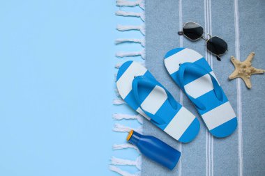 Şık plaj ayakkabıları, havlu ve mavi arka planda bir şişe güneş kremi, yakın plan.
