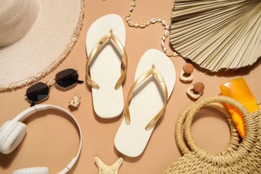 Bej arka planda şık plaj ayakkabıları, kulaklıkları ve aksesuarları olan kompozisyon, yakın plan.