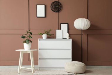 Oturma odasının içinde çekmeceler, masa ve puf kahverengi duvarın yanında.