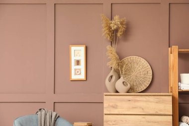 Oturma odasının iç tarafındaki kahverengi duvarın yanındaki çekmecelerin üzerinde otlar olan vazolar, yakın plan.