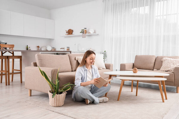 молодая женщина, сидящая на полу и читающая книгу в светлой гостиной