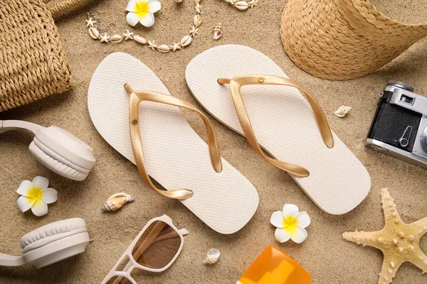 Plaj ayakkabıları, aksesuarları ve kulaklıklı kompozisyon arka plan olarak kumda, yakın plan