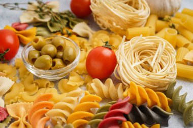 Farklı pişmemiş makarna, zeytin ve domatesler masada, yakın plan.