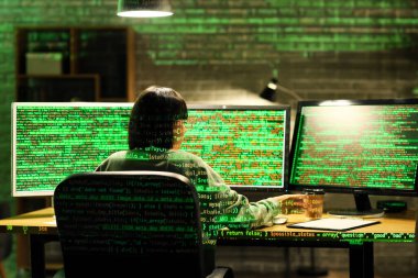 Bilgisayar monitörleriyle çalışan kadın programcı gece ofiste, arka planda