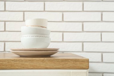 Beyaz tuğla duvarın yanındaki ahşap masada yığınla temiz sofra takımı var.