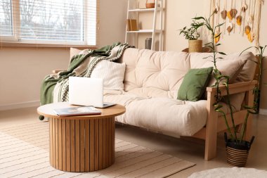 Ekoseli rahat kanepe, dizüstü bilgisayarlı kahve masası ve oturma odasında bambu bitkisi.