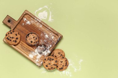 Çikolata parçalı ahşap kurabiye tahtası ve yeşil zemin üzerinde undan yapılmış kalp.