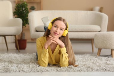 Kulaklıklı, müzik dinleyen ve şık bir oturma odasında yerde yatan genç ve güzel bir kadın.