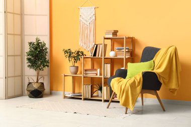 Rahat koltuğu, saksısı, raf ünitesi ve sarı ekoseli güzel bir oturma odası.