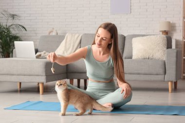 Evde yoga minderinde kedi yavrusuyla oynayan genç bir kadın.