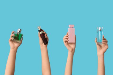 Mavi arka planda farklı parfüm şişeleri olan kadın elleri.