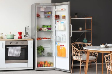 Mutfaktaki beyaz duvarın yanında taze yiyeceklerle dolu bir buzdolabı.