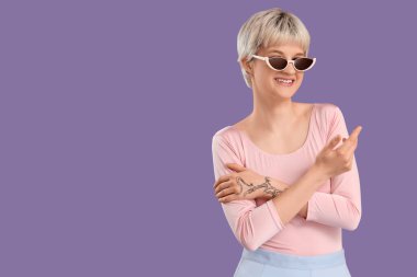 Portrait of beautiful young woman with sunglasses on lilac background