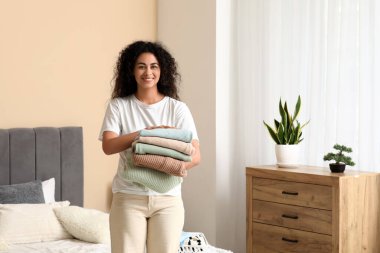 Güzel, genç, mutlu, Afro-Amerikan kadın. Yatak odasında bir yığın temiz giysi var.