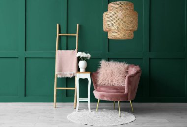 Pembe koltuk ve yeşil duvarın yanındaki çiçekli kahve masası.