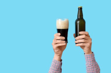 Mavi arka planda şişeli eller ve bir bardak bira.