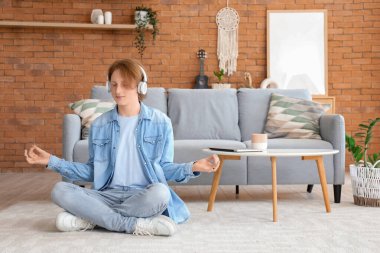 Kulaklıklı kızıl saçlı genç çocuk evde meditasyon yapıyor.