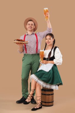 Geleneksel Alman kıyafetleri içinde, bej arka planda oturan, çerez, fıçı ve bira dolu genç mutlu bir çift.