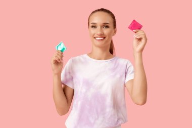 Pembe arka planda prezervatifli genç bir kadın.