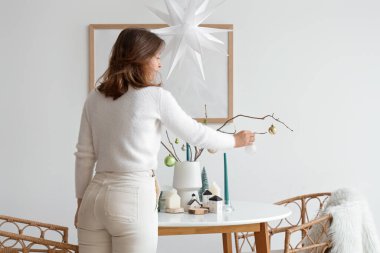 Yemek odasındaki ağaç dallarında Noel topları olan genç bir kadın.